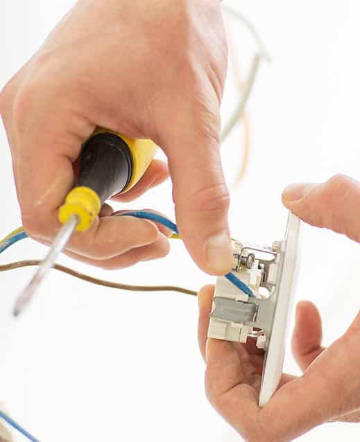 Électricien en train de raccorder des fils électriques sur un interrupteur avec un tournevis