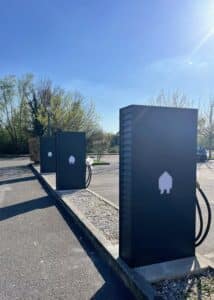 Bornes de recharge pour véhicules électriques noires au design épuré sur un parking sous un ciel bleu ensoleillé.
