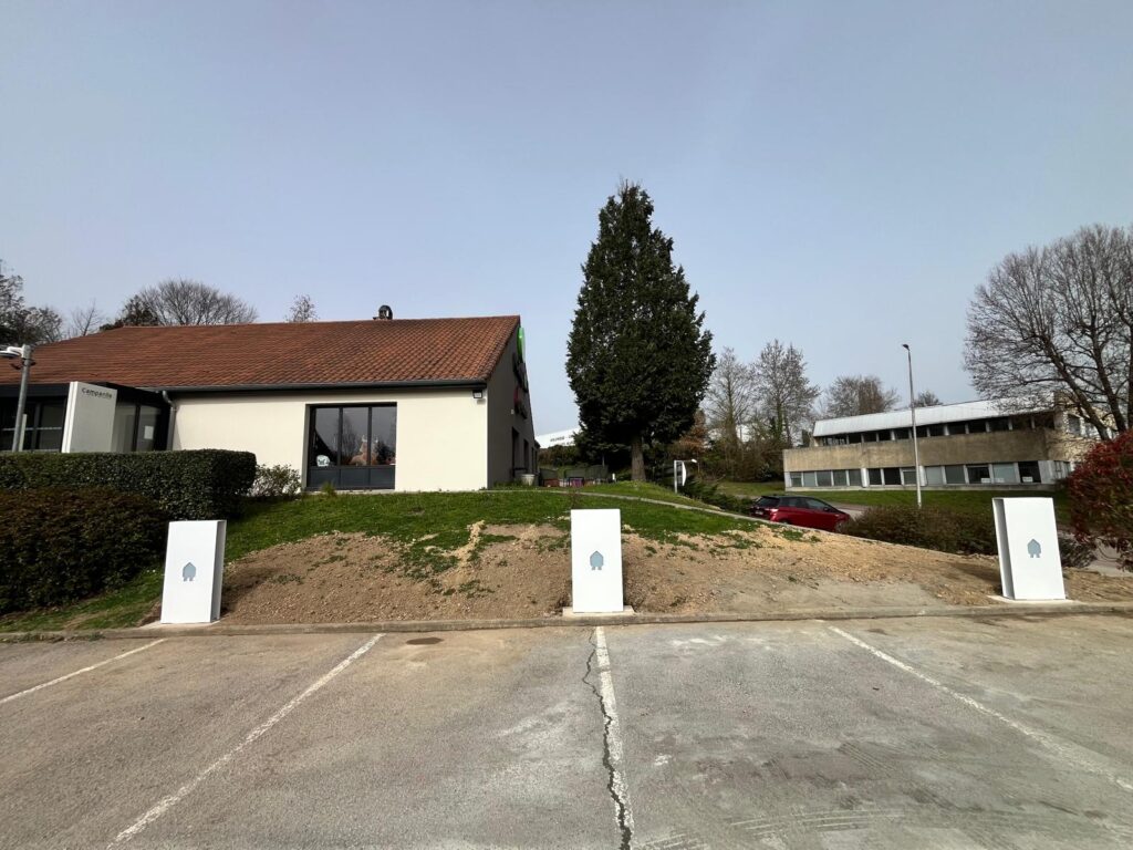 Trois bornes de recharge électrique blanches devant l'hôtel Campanile avec son parking et ses espaces verts.